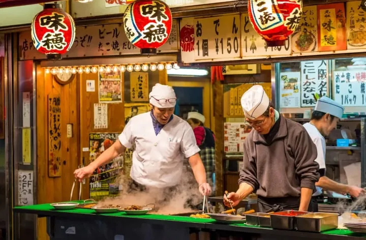 赤い提灯の下でたこ焼きを焼く屋台の料理人たち